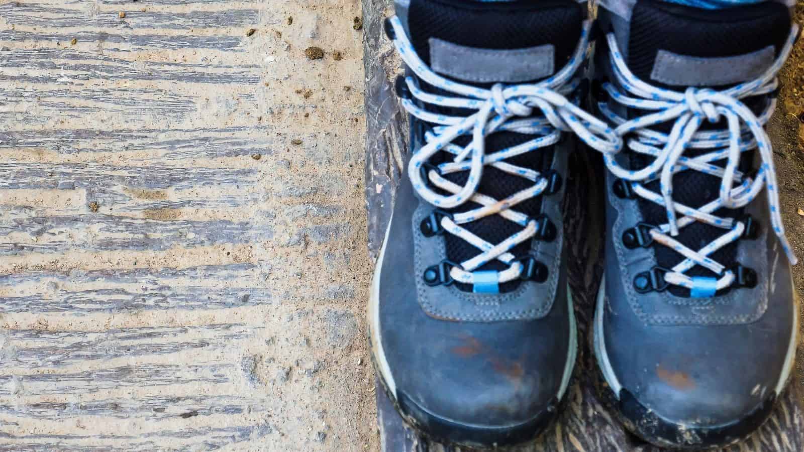 Worn blue hiking boots with white laces stand on a rough, textured concrete surface, ready to face unpredictable weather—true travel essentials for any hiking adventure.