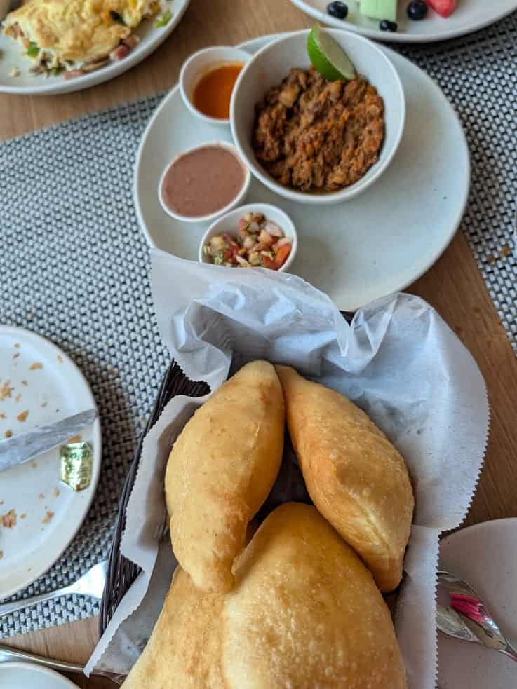 A basket of fried bread with dips and a bowl of shredded meat on a table set for a meal, evoking the flavors you might discover during a Belize reef and ruins trip.