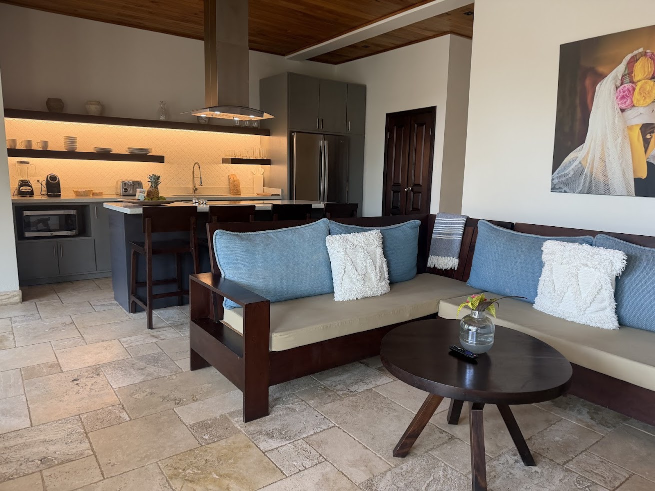 Modern kitchen and living area with blue cushions, wood furniture, and wall art of a woman with flowers&mdash;an inviting atmosphere reminiscent of spaces featured in a glowing The Lodge at Jaguar Reef review.