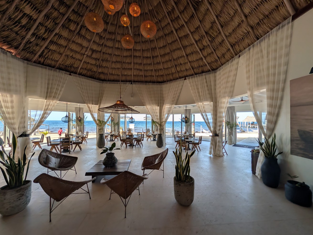 Open-air beachside lounge with wicker chairs, potted plants, and ocean view under a thatched roof&mdash;an ambiance frequently highlighted in The Lodge at Jaguar Reef review for its relaxed elegance and tropical charm.