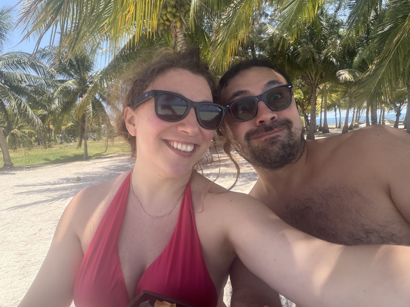 Two people in sunglasses smile under palm trees on a sunny beach, enjoying a tropical day together&mdash;an experience reminiscent of the glowing praise found in every The Lodge at Jaguar Reef review.