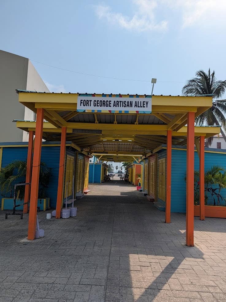 Colorful entrance to Fort George Artisan Alley with closed shops, palm trees, and a clear blue sky&mdash;a perfect starting point for your Belize reef and ruins trip.