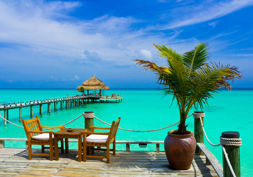 Wooden deck with a table, chairs, palm tree, and a pier over bright turquoise ocean under a blue sky&mdash;an ideal setting to relax and dream up your list of things to do in Cartagena.