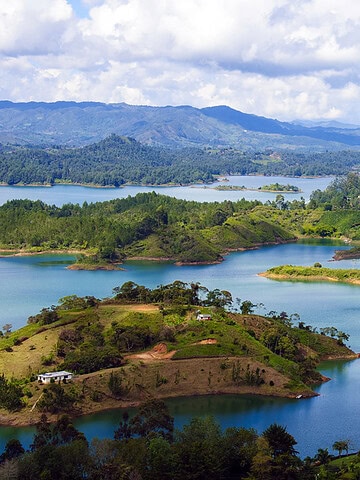 Lush green islands and a white building on a turquoise lake with mountains and clouds in the background create a scene reminiscent of the natural beauty you can explore while discovering things to do in Medellin with kids.