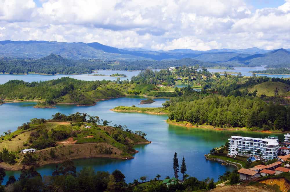 Lush green islands and a white building on a turquoise lake with mountains and clouds in the background create a scene reminiscent of the natural beauty you can explore while discovering things to do in Medellin with kids.