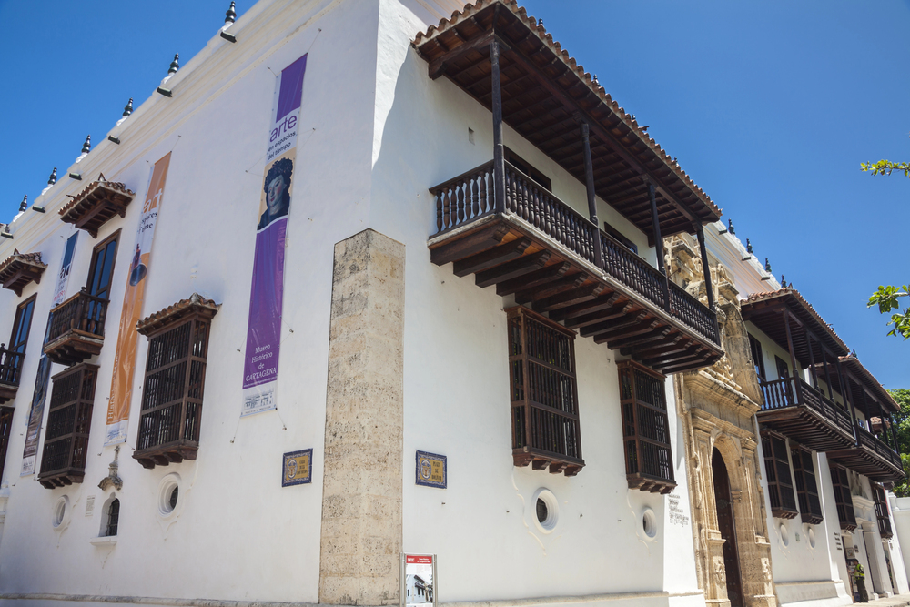 White colonial building with wooden balconies, banners, and a stone entrance against a clear blue sky&mdash;an iconic sight among the many things to do in Cartagena.