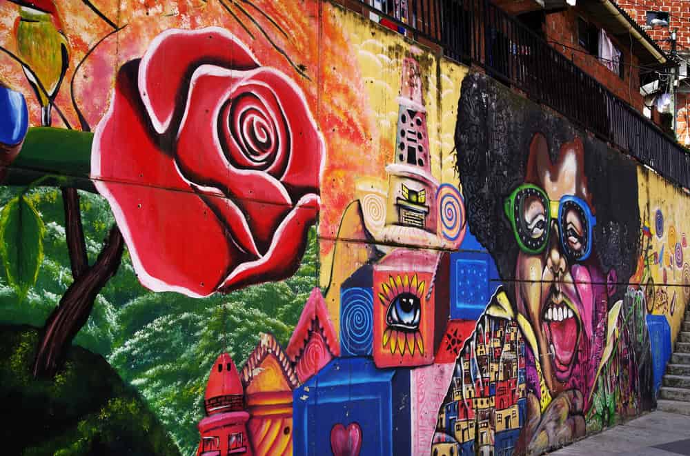 Colorful mural with a large red rose, abstract faces, and vibrant cityscape elements on a concrete wall—an inspiring sight that’s perfect for families exploring unique Things to Do in Medellin with Kids.