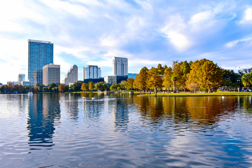 City buildings and autumn trees reflect on a calm lake under a bright, partly cloudy sky, creating a serene scene that’s perfect for families searching for things to do in Orlando with kids.