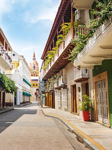 Colorful colonial buildings line an empty street under a blue sky, with a church tower in the distance—a picturesque scene that perfectly captures the charm you’ll discover among the many things to do in Cartagena.