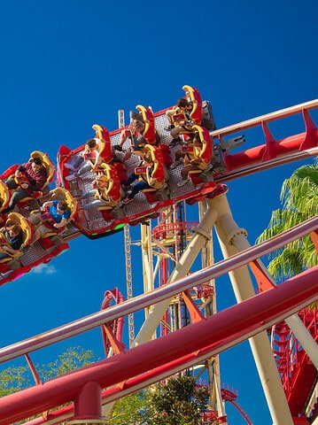 People ride a red roller coaster under a bright blue sky with a few white clouds and green trees nearby—a thrilling highlight among the top things to do in Orlando with kids.