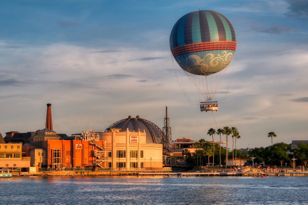 A striped hot air balloon floats above a waterfront cityscape at sunset, with palm trees and buildings below—capturing the sense of adventure that makes it one of the unforgettable things to do in Orlando with kids.