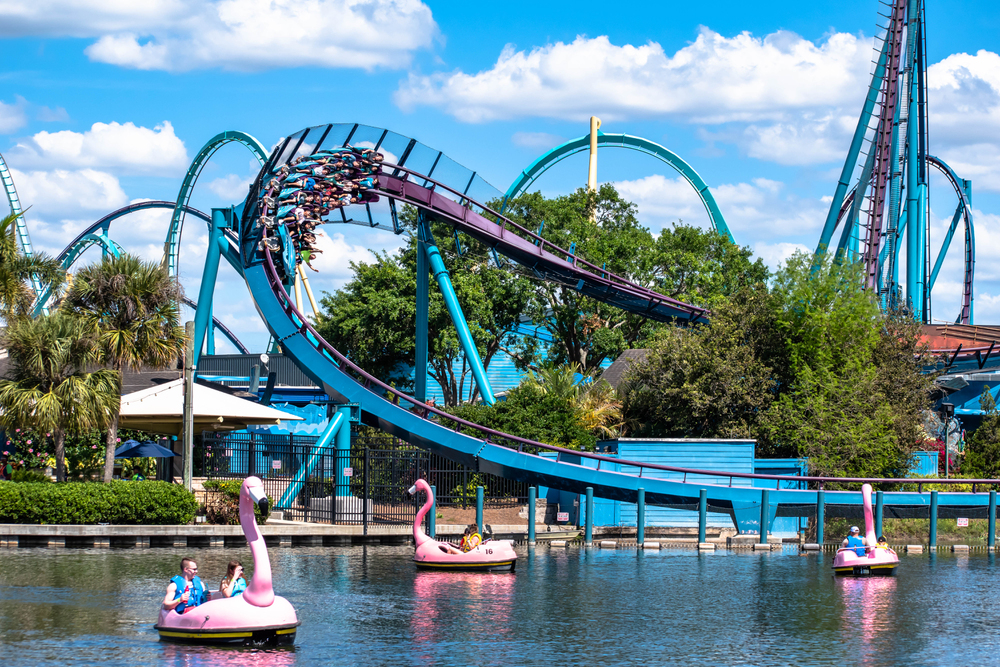 A roller coaster passes above a pond with pink flamingo paddle boats and people riding them, making it one of the most fun things to do in Orlando with kids.