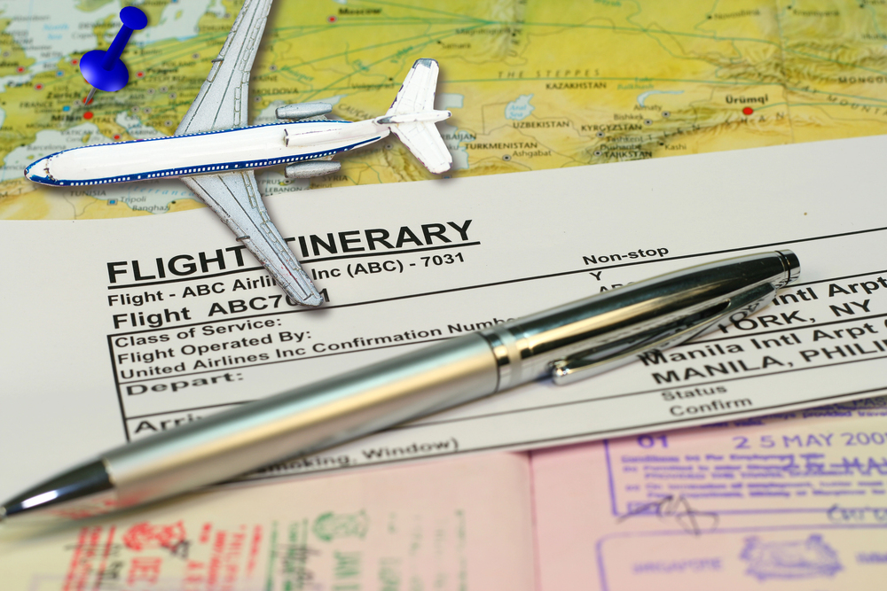A flight itinerary, pen, and toy airplane sit on a map with travel documents and a blue pushpin&mdash;capturing the spirit of empty nest travel and new adventures ahead.