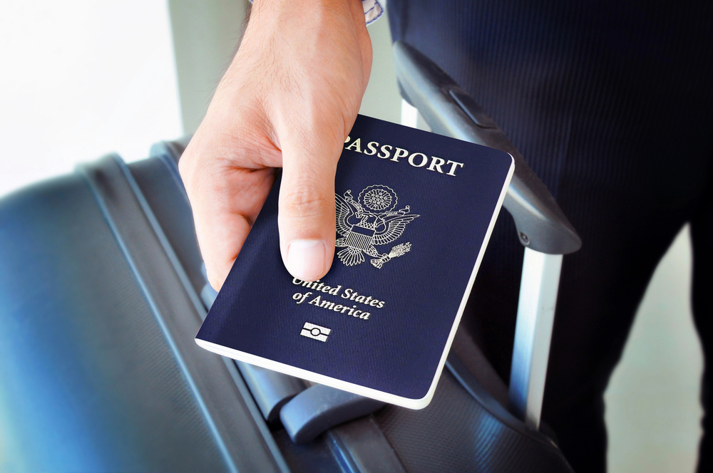 A person holding a U.S. passport next to the handle of a black suitcase, ready for their next empty nest travel adventure.