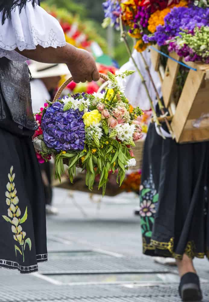Person carrying a basket of colorful flowers, wearing traditional embroidered clothing at a festival—one of the delightful sights you may encounter while exploring things to do in Medellin with kids.