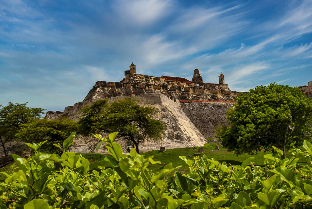 Stone fortress stands on a hilltop, surrounded by greenery, under a bright blue sky with wispy clouds&mdash;a must-see among the many things to do in Cartagena.