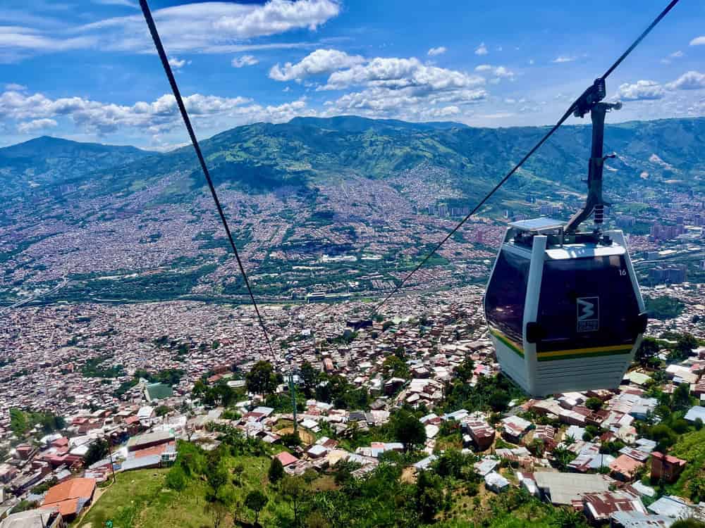 A cable car ascends over a city with mountains and scattered clouds in the background, offering a unique perspective and making it one of the top things to do in Medellin with kids.