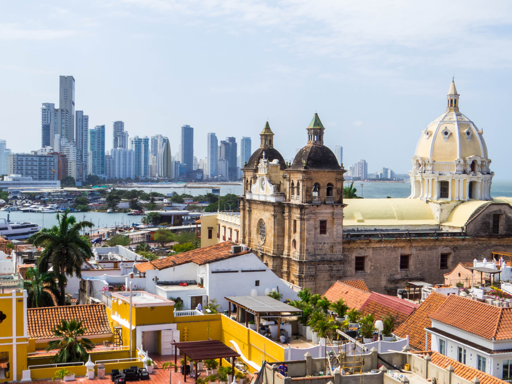 Historic church with domed roof, colorful buildings, and modern city skyline in the background&mdash;a perfect spot to add to your list of things to do in Cartagena.