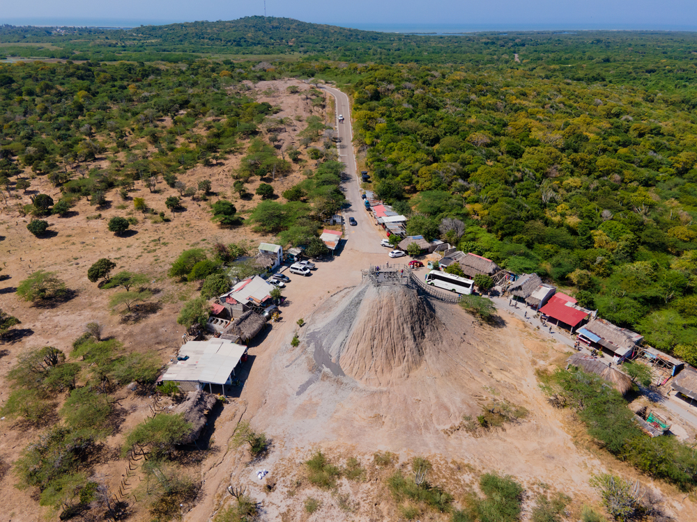 Aerial view of a large mud volcano surrounded by small houses and greenery in a rural area&mdash;one of the unique things to do in Cartagena for adventurous travelers seeking natural wonders beyond the city.