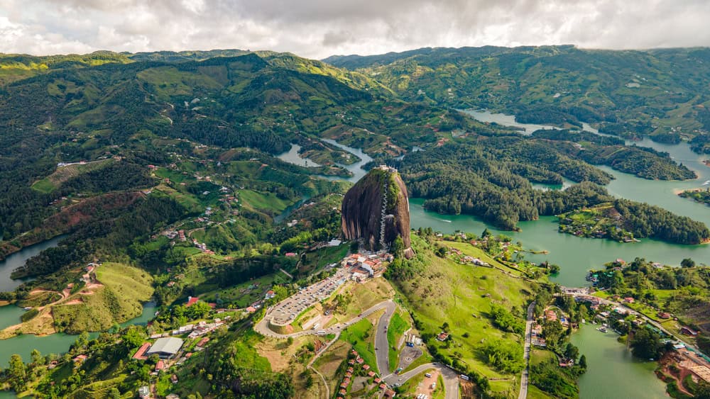 Aerial view of a large rock formation surrounded by green hills, lakes, and scattered buildings—a stunning destination and one of the top Things to Do in Medellin with Kids.