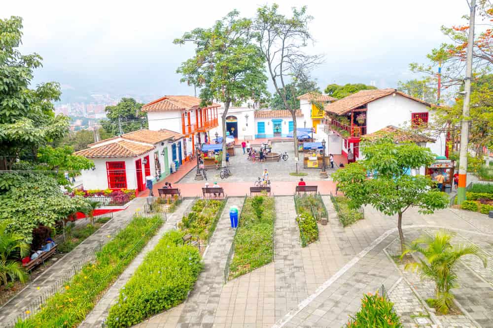 Colorful colonial buildings surround a small plaza with benches, trees, and pathways in a hillside town—making it an ideal spot for families looking for things to do in Medellin with kids.