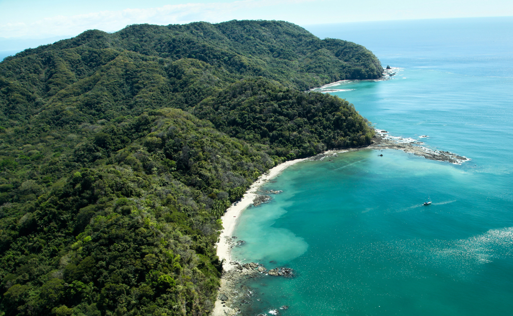 Aerial view of a lush green coastline with turquoise water and small boats near the shore—an ideal destination to travel with teens, offering adventure and vibrant scenery for unforgettable family memories.