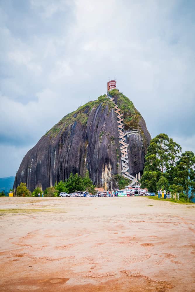 Large rock with zigzag stairs, people and cars at base, cloudy sky, some trees visible around the rock—a perfect spot to add to your list of things to do in Medellin with kids.