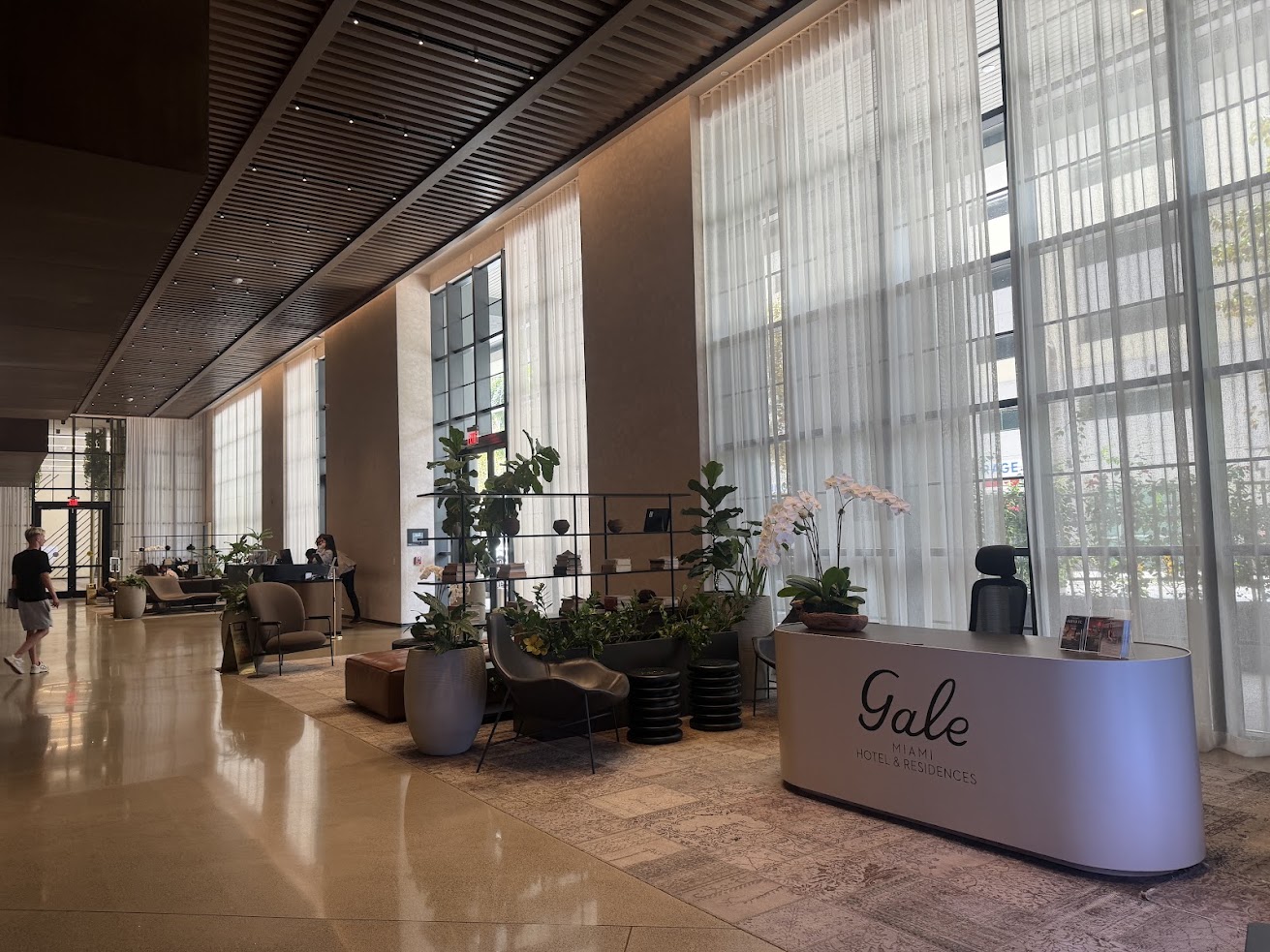 Spacious hotel lobby with tall windows, plants, seating area, and a Gale Miami desk near the entrance—an inviting space often highlighted in many Gale Miami Hotel & Residences reviews.