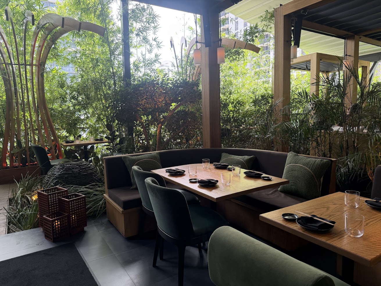 A cozy restaurant patio with green chairs, wooden tables, and lush plants surrounding the seating area—an inviting atmosphere reminiscent of those highlighted in a Gale Miami Hotel & Residences review.