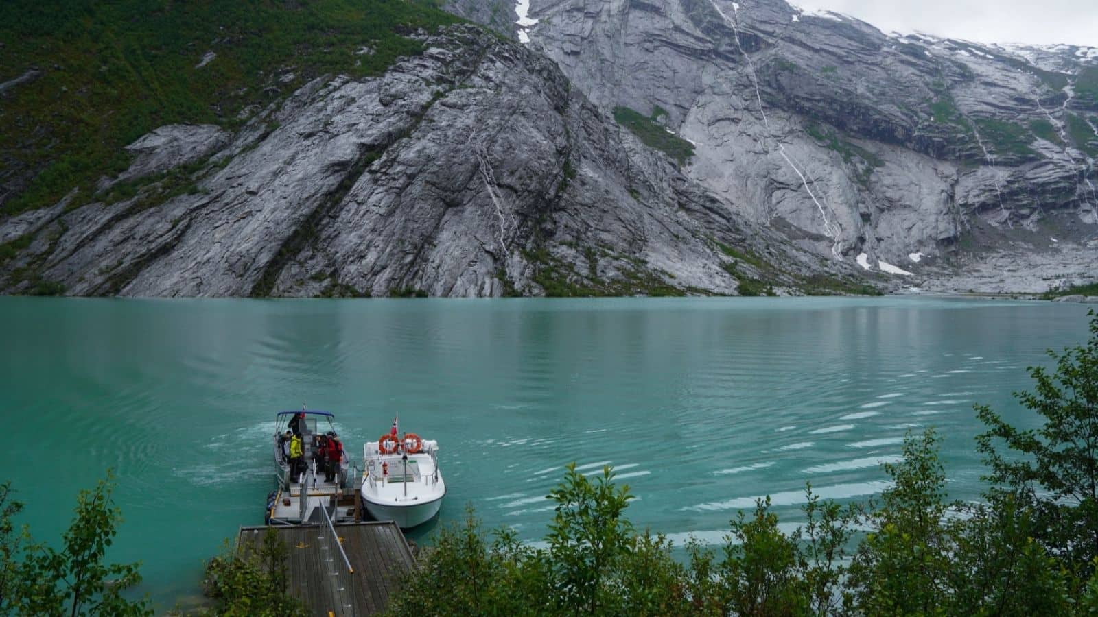A small boat docked on turquoise water with rocky mountains and greenery in the background.