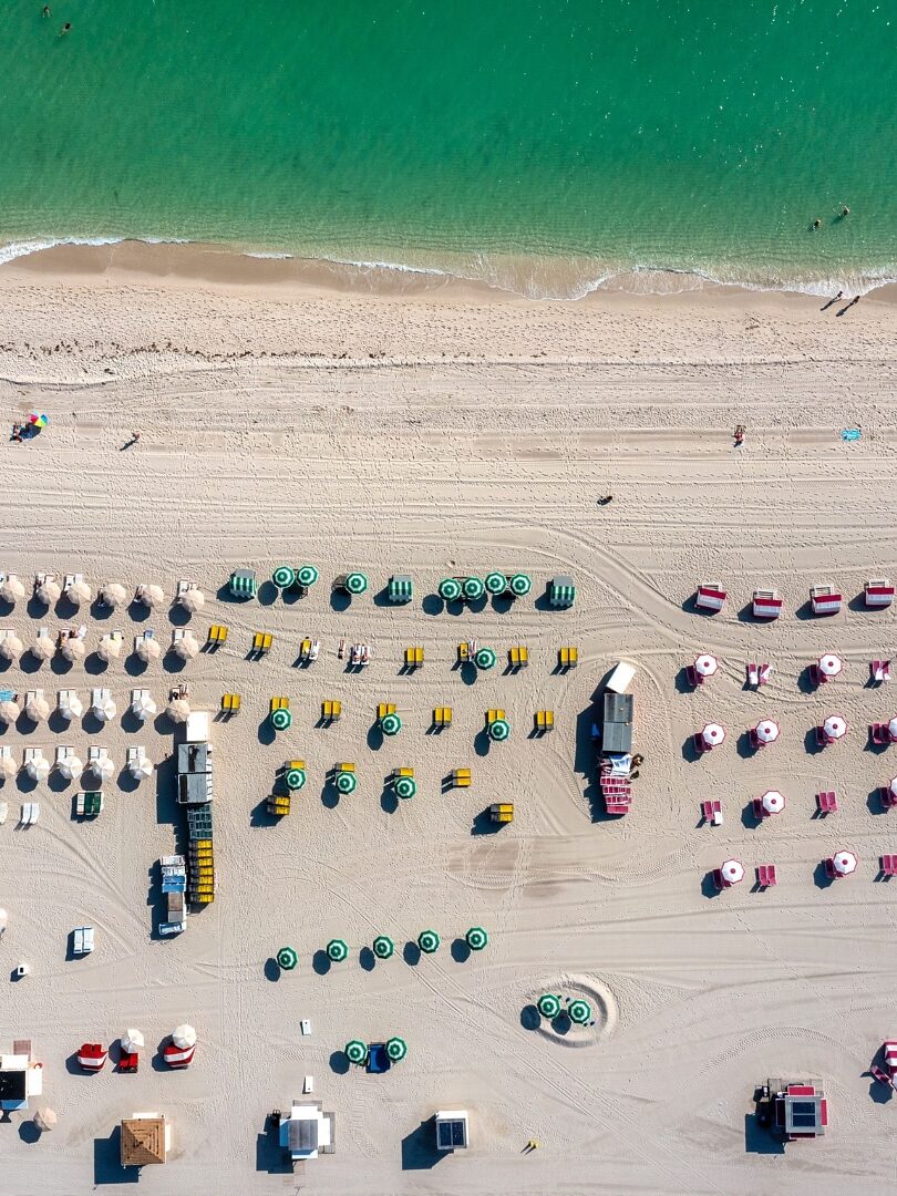 Aerial view of a beach with colorful umbrellas and chairs on white sand next to turquoise water, reminiscent of the vibrant scenes described in many Gale Miami Hotel & Residences reviews.