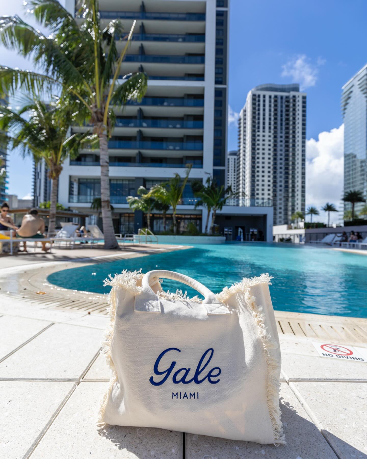 A white tote bag reading “Gale Miami” sits poolside, with tall buildings and palm trees in the background, perfectly capturing the relaxed vibe mentioned in our Gale Miami Hotel & Residences Review.