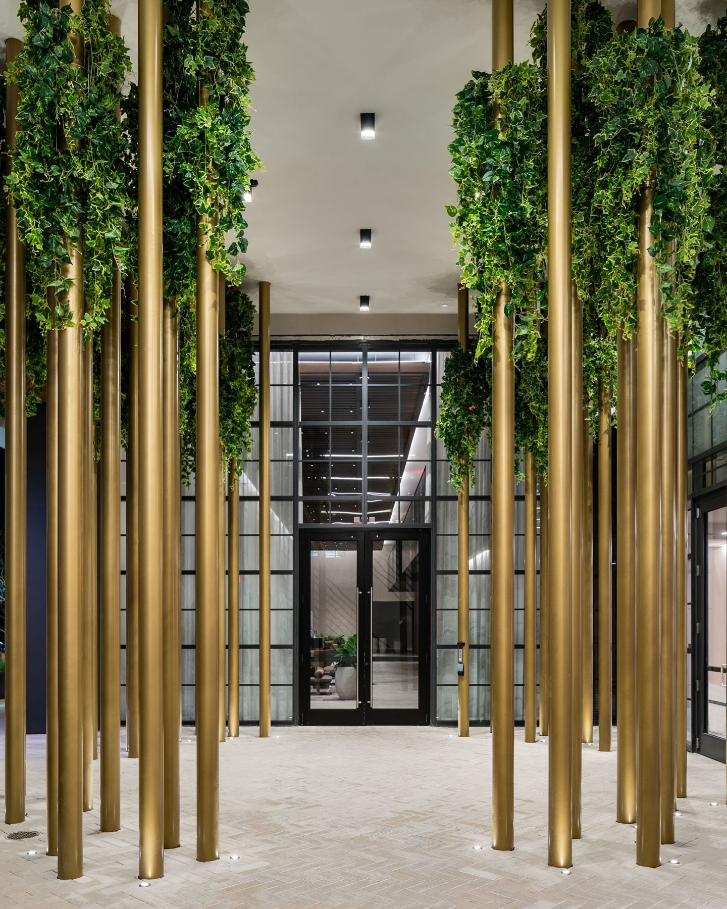 Tall golden poles with green foliage line a modern indoor walkway at the Gale Miami Hotel & Residences, leading to glass doors in the background—setting the scene for a sophisticated review of this stylish destination.