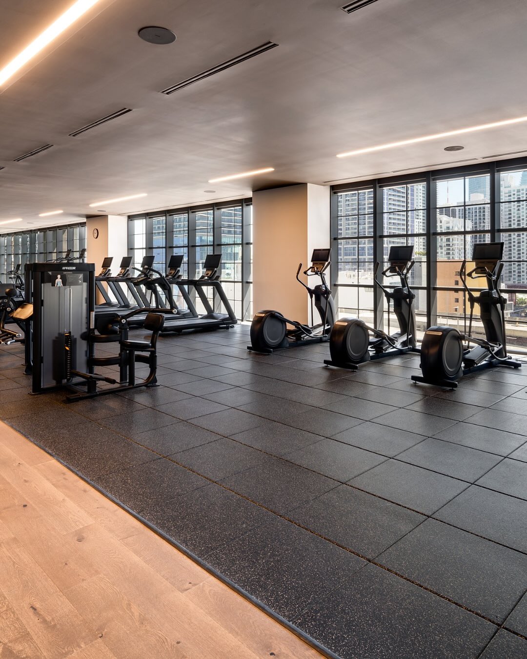 Modern gym with treadmills, ellipticals, and strength machines near large windows overlooking a cityscape—an amenity frequently highlighted in a Gale Miami Hotel & Residences review.