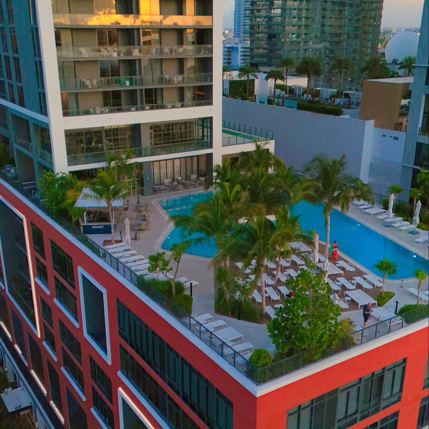A rooftop pool surrounded by palm trees and lounge chairs atop a modern city building at sunset sets the scene for a perfect evening, as highlighted in many Gale Miami Hotel & Residences reviews.