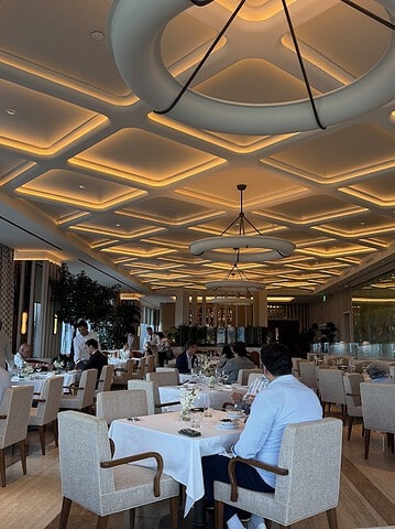 Diners sit at tables in an elegant Seia Miami restaurant with a geometric, backlit ceiling.