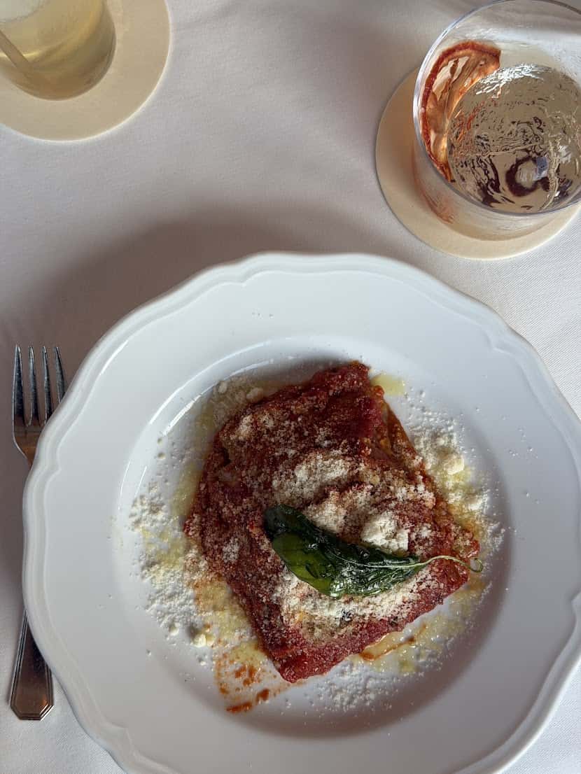 A square of lasagna topped with basil and cheese on a white plate, captured for a Seia Miami review.