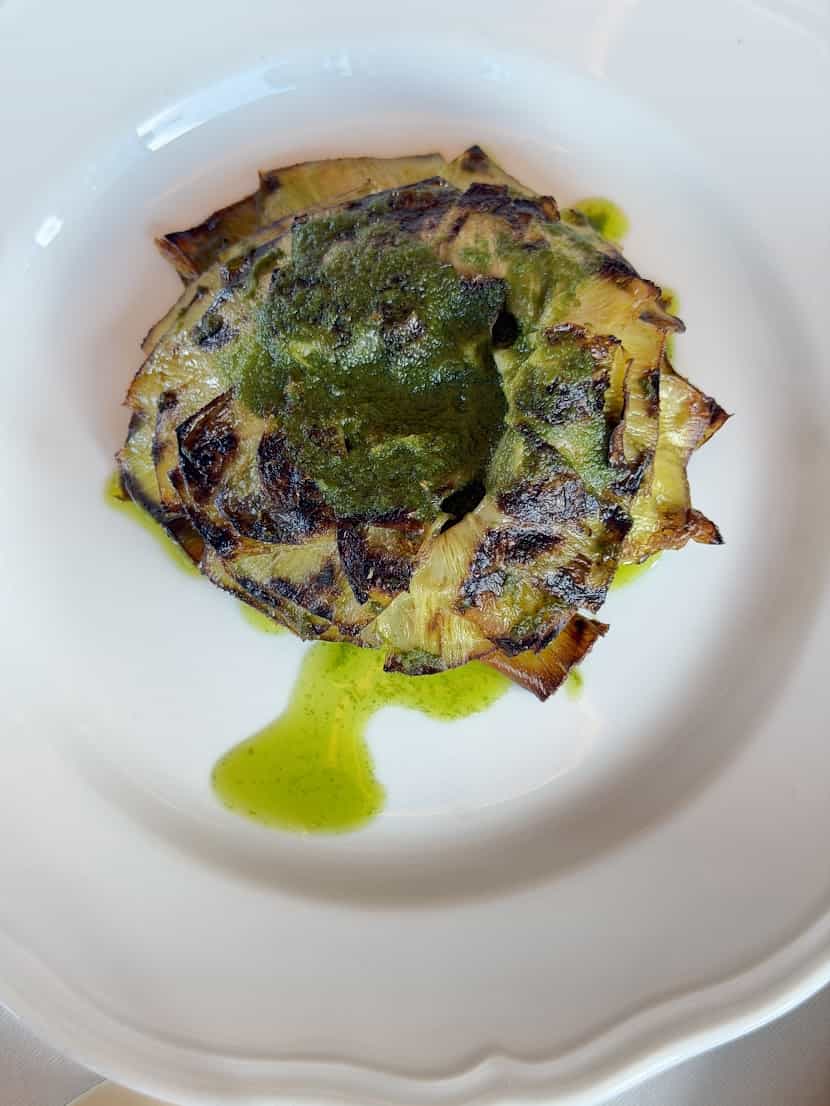 Grilled artichoke drizzled with green herb sauce on a white plate, served at Seia Miami.