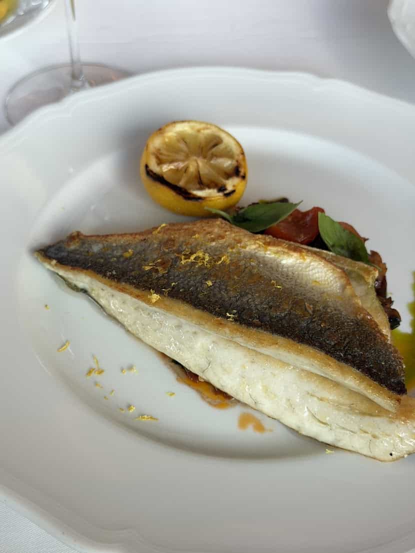 Pan-seared fish fillet with a grilled lemon half and herbs on a white plate, as seen in the Seia Miami review.