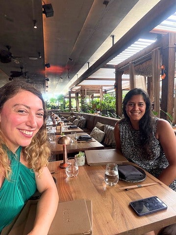Two women smiling at a table during a Mila Miami review at an open-air restaurant.