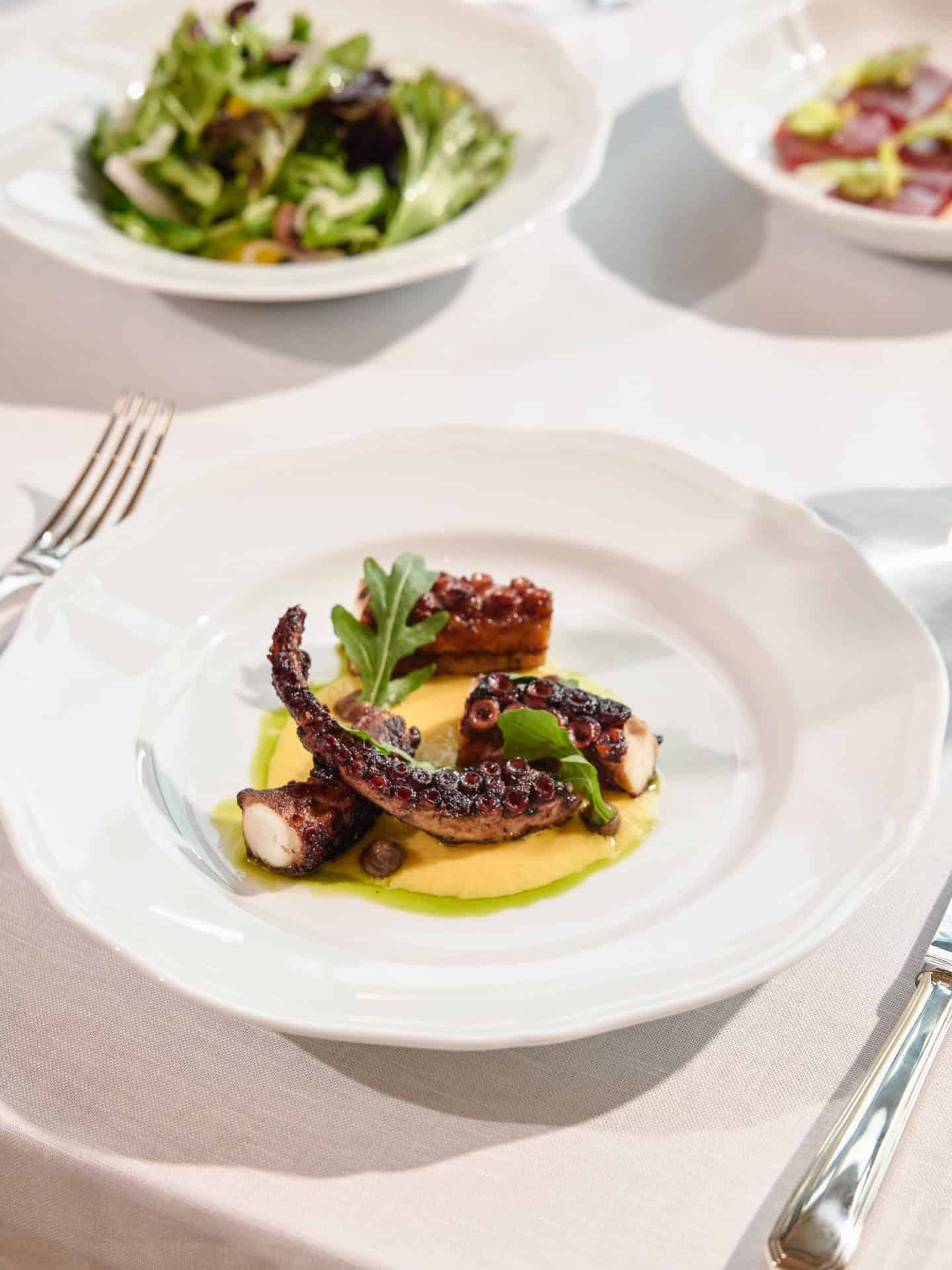 Grilled octopus tentacle on yellow puree with greens, as seen in a Seia Miami review.