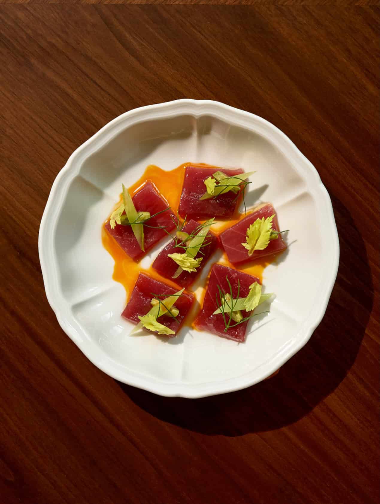 Five square slices of raw tuna for a Seia Miami review, drizzled with oil and garnished with celery in a white bowl.