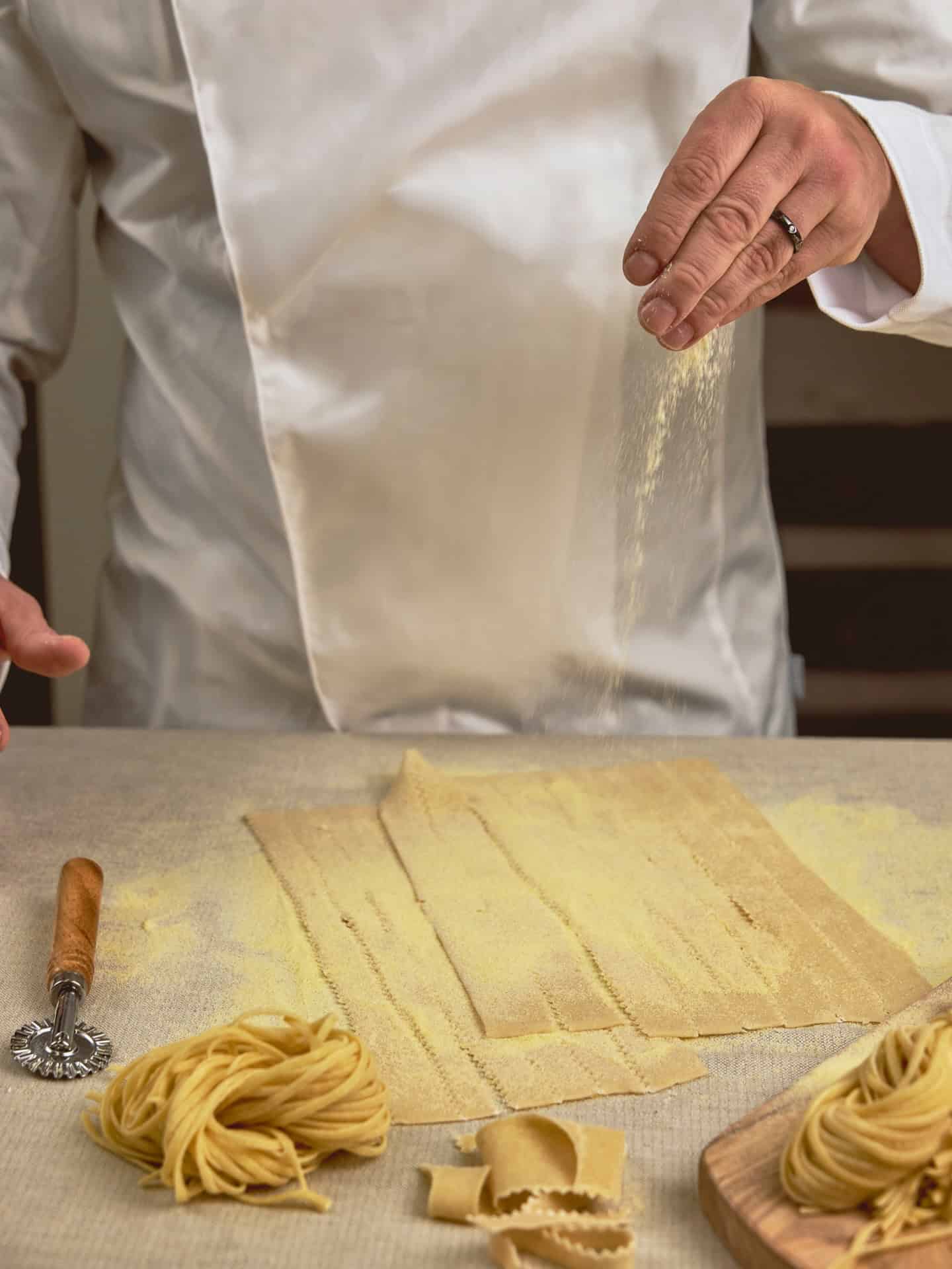 A chef in a white uniform sprinkles flour over fresh pasta sheets for a Seia Miami review.