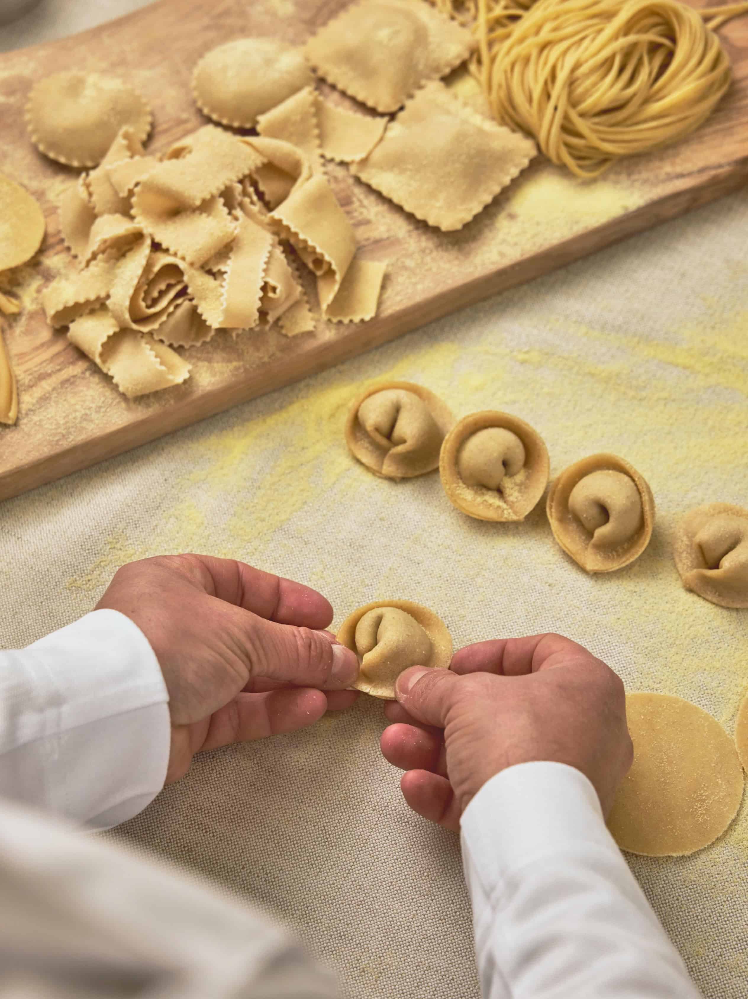 Hands forming fresh tortellini on a floured surface, reminiscent of the pasta seen in a Seia Miami review.
