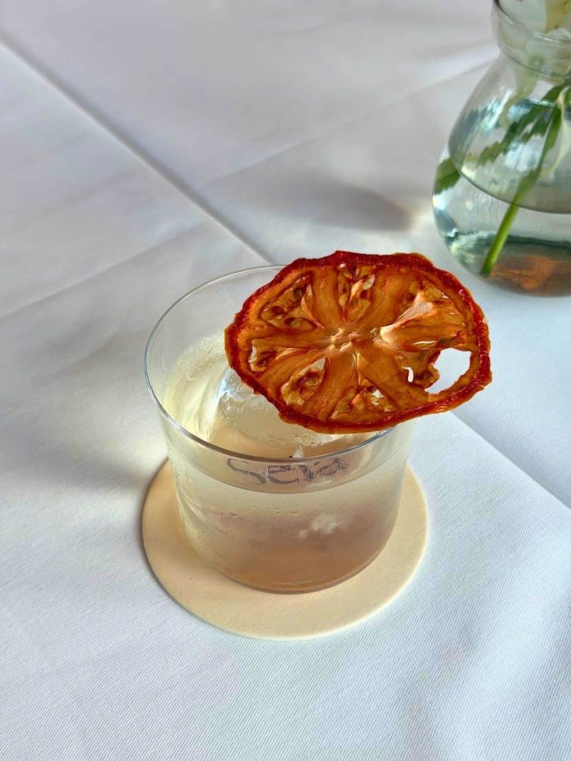 A cocktail in a glass with a large ice cube and a dehydrated citrus slice, as seen in a Seia Miami review.
