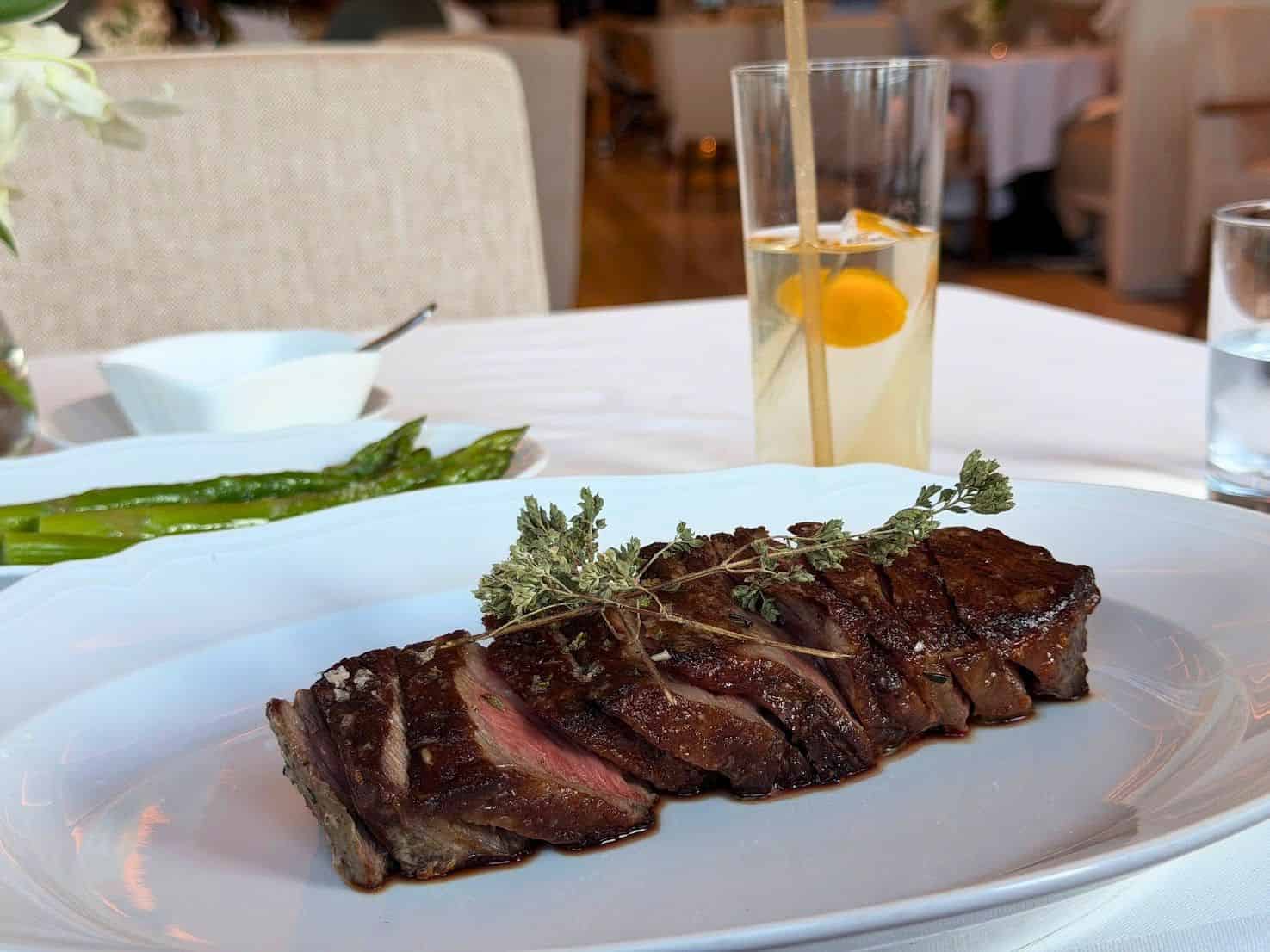 Sliced steak with herbs and asparagus on a white plate, as seen in a Seia Miami review.