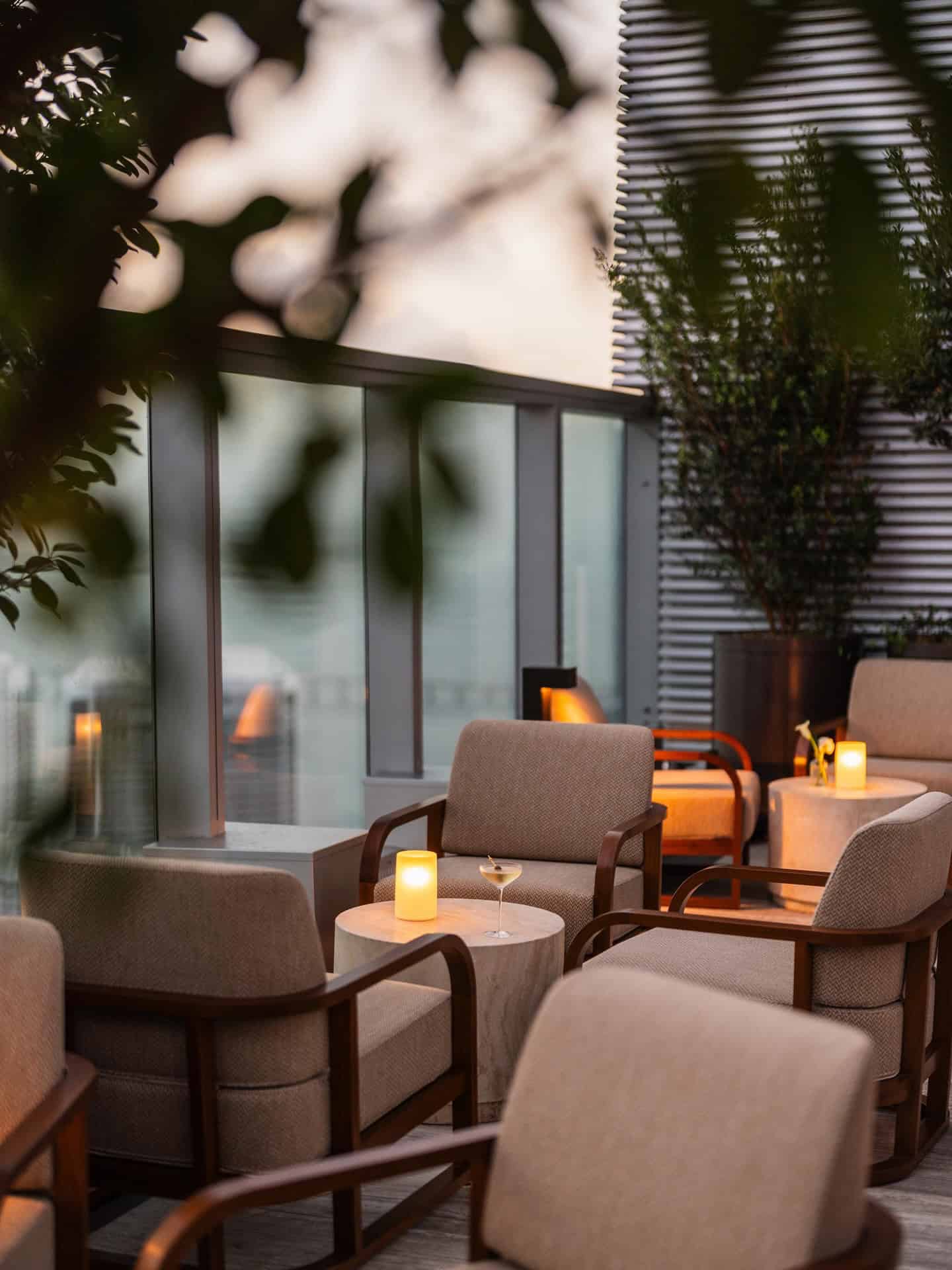 Twilight view of an outdoor lounge area at Seia Miami with upholstered armchairs, small tables, and lit candles.