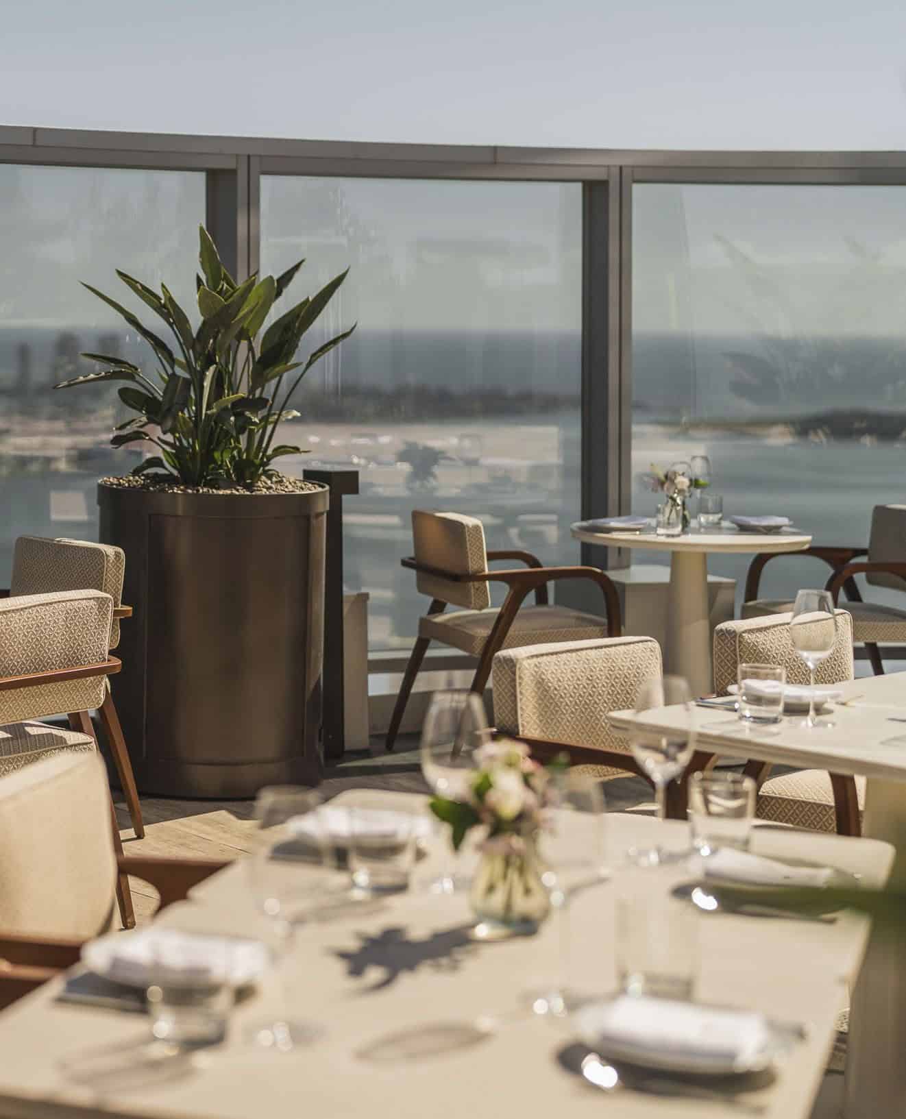Dining tables and chairs on a rooftop terrace overlooking the sea, as seen in a Seia Miami review.