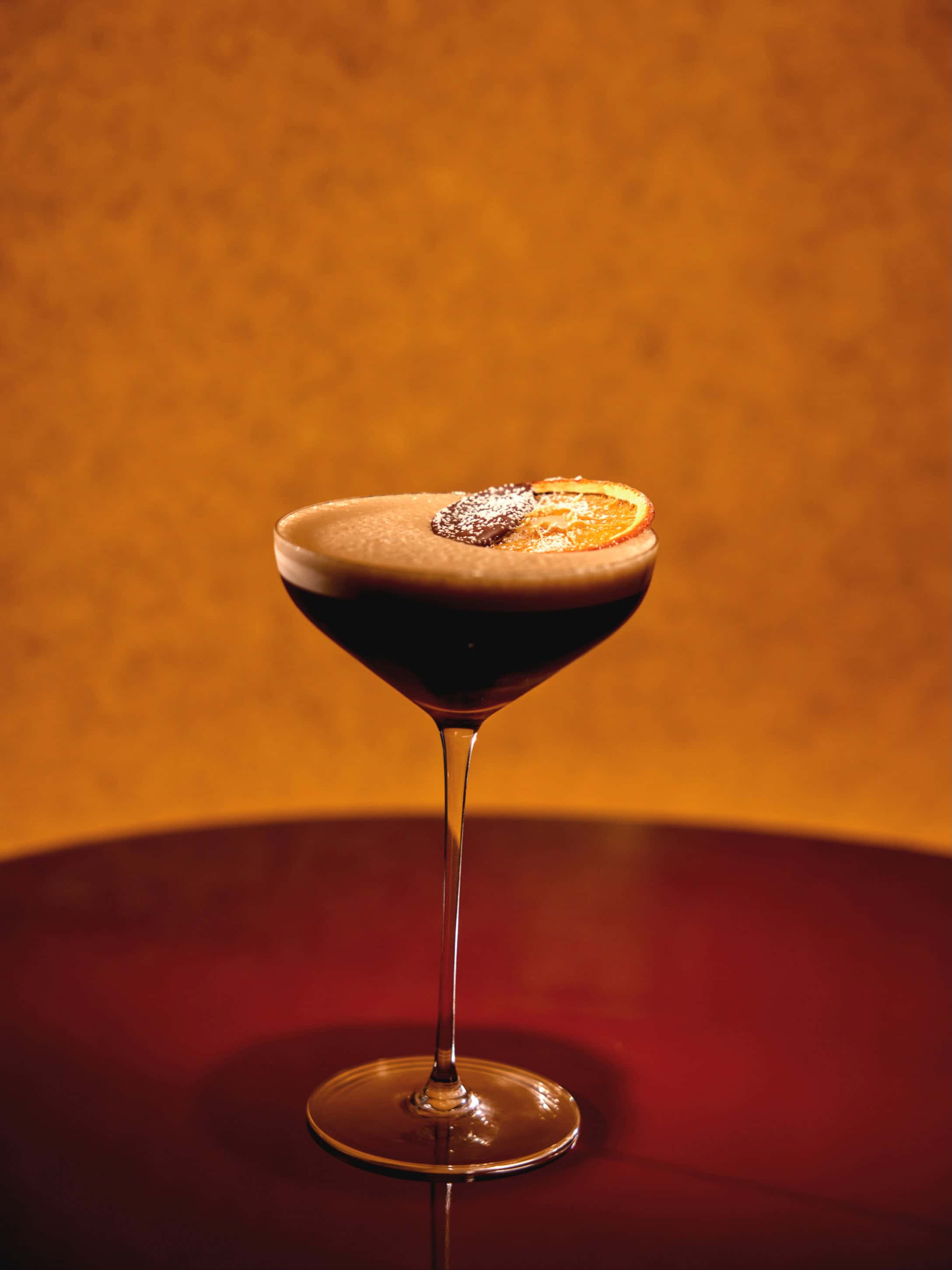 A dark cocktail in a coupe glass, garnished with a chocolate-dipped orange slice, captured for a Seia Miami review.